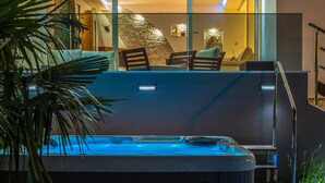 Quarto de hotel moderno com varanda envidraçada, hidromassagem e parede de pedra.