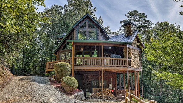 Une cabane en rondins à deux étages, dotée d’un balcon et entourée d’une forêt dense.
