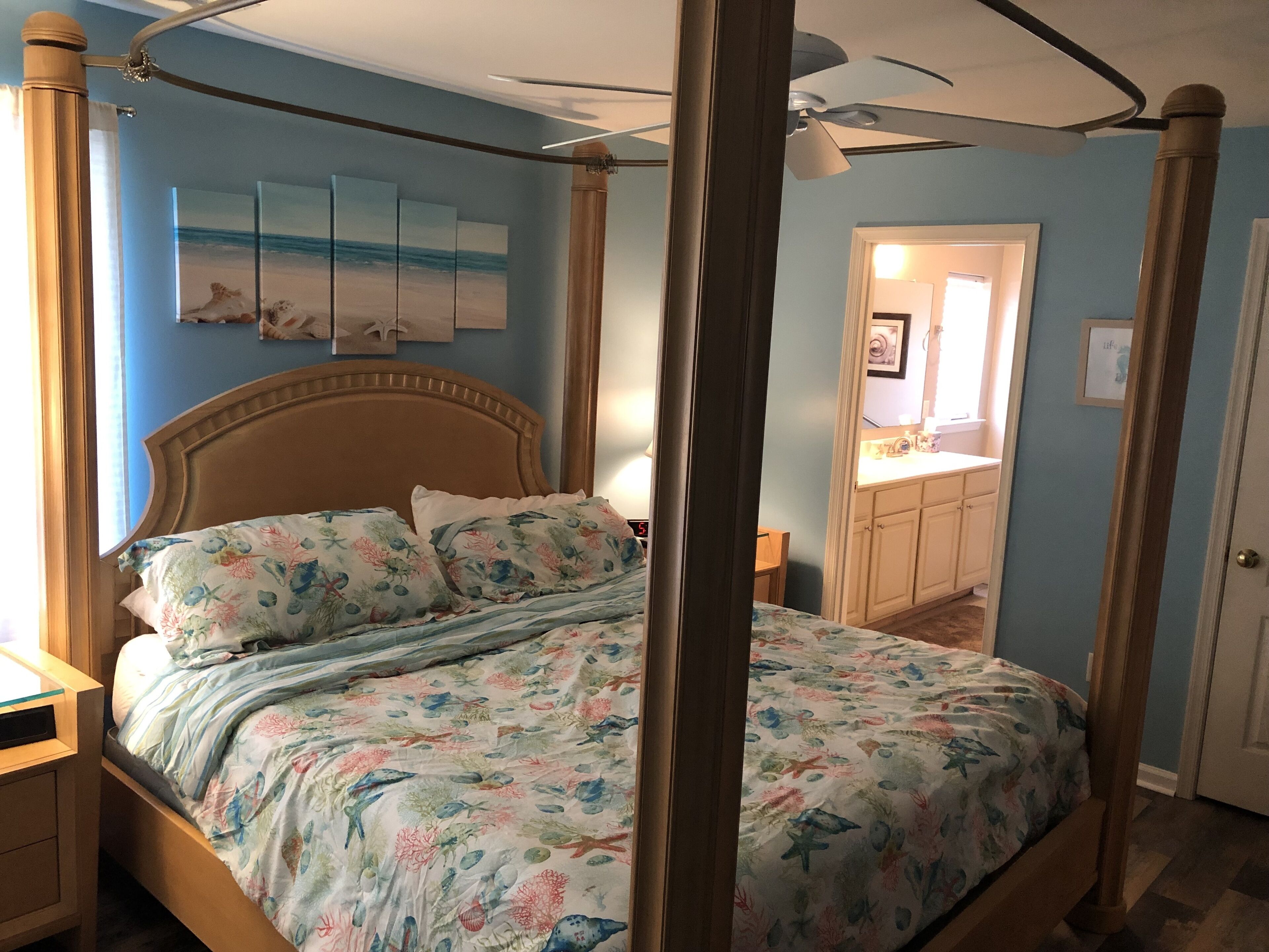 A four-poster bed with a floral bedspread, a wooden headboard, and a ceiling fan.