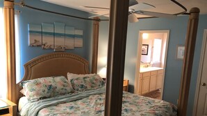 A four-poster bed with a floral bedspread, a wooden headboard, and a ceiling fan. - 4106 Palms, 1st floor, 3-bedroom, 2-bath, Aug and Sept weekends still available (Rehoboth Beach)