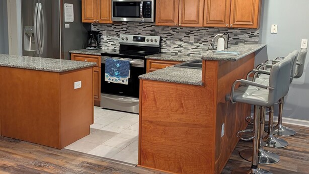 A modern kitchen with wooden cabinets, stainless steel appliances, and a granite countertop. - 4106 Palms, 1st floor, 3-bedroom, 2-bath, Aug and Sept weekends still available (Rehoboth Beach)