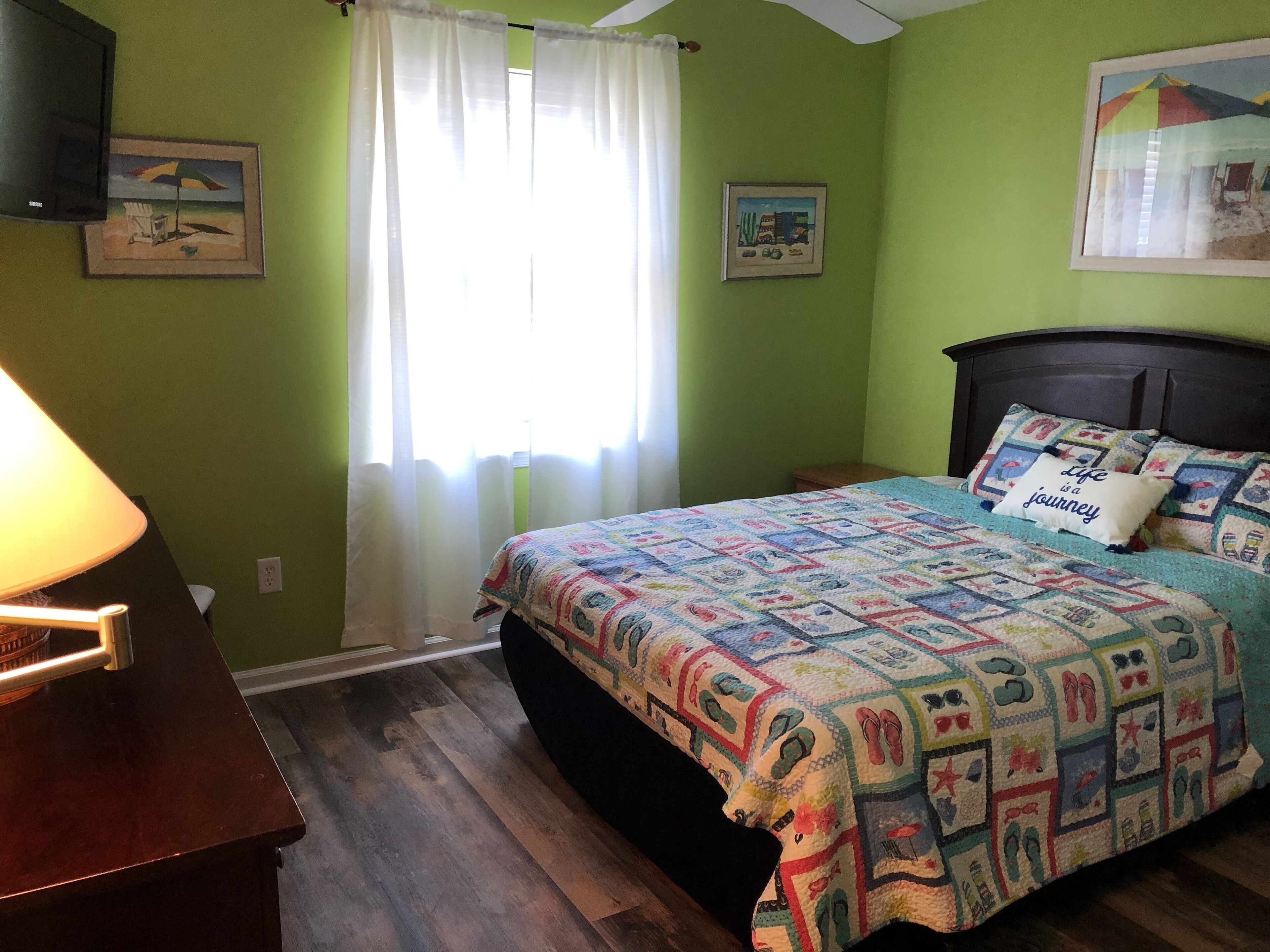 A bedroom with a bed, a nightstand, a lamp, a window with curtains, and two wall art pieces.