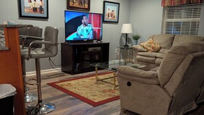 A living room with a television, a sofa, a coffee table, and a dining area with chairs. - 4106 Palms, 1st floor, 3-bedroom, 2-bath, Aug and Sept weekends still available (Rehoboth Beach)