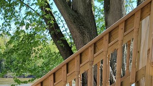 Eine Holztreppe führt zu einem betonbestreuten Weg entlang eines Gewässers, umgeben von Bäumen.