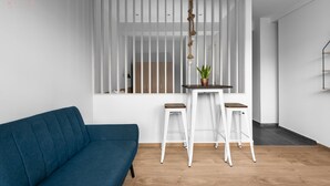 Ein modernes Wohnzimmer mit einem blauen Sofa, einem weißen Essbereich mit zwei Hocker und einem Holzboden.