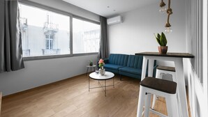 Ein modernes Wohnzimmer mit einem blauen Sofa, einem runden Couchtisch mit Blumenvase und einem weißen Barhocker.