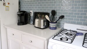 A kitchen with a white countertop, a toaster, a coffee maker, a stove, and a blue and white patterned container holding utensils. - Charming getaway in the heart of historic Hancock Neighborhood. (Austin)