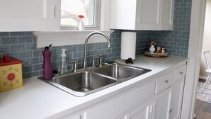 A kitchen with white cabinets, a double sink, and a window with a vase of flowers. - Charming getaway in the heart of historic Hancock Neighborhood. (Austin)