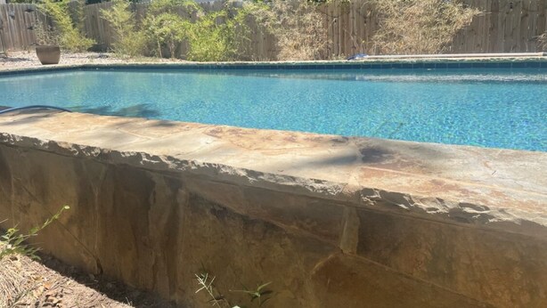 A swimming pool with a stone border, surrounded by a wooden fence and vegetation. - Charming getaway in the heart of historic Hancock Neighborhood. (Austin)