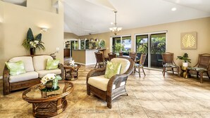 A spacious living area with wicker furniture, a glass coffee table, and a view of the kitchen and outdoor patio.