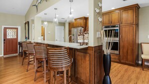 A kitchen with wooden cabinets, a stainless steel refrigerator, and a bar area with stools.