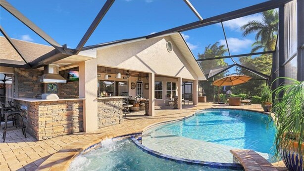 A swimming pool with a hot tub, outdoor bar, and stone-tiled deck.