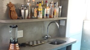 Una cocina con un lavamanos empotrado, una licuadora y estantes llenos de botellas y frascos.