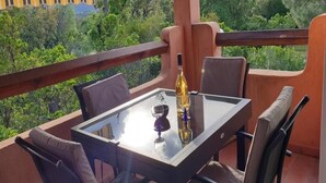 Een balkon met een glazen tafel, vier stoelen en een fles wijn.