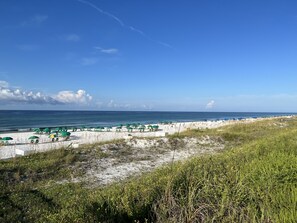 A beach with white sand, green umbrellas, and a clear blue sky.