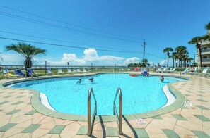 Una piscina con borde de baldosas, rodeada de sillas de descanso y palmeras.