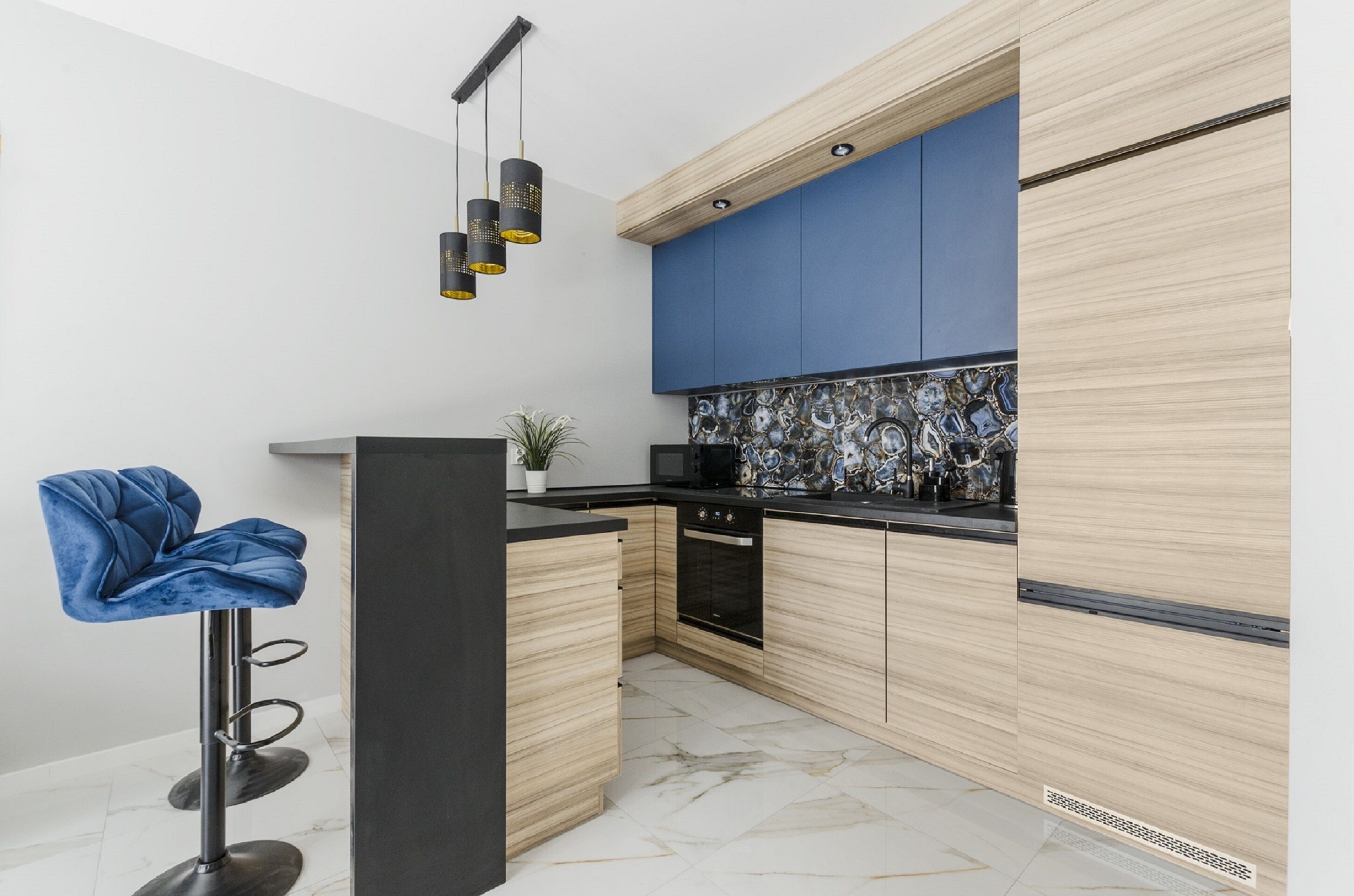 Une cuisine moderne avec des meubles en bois, un plan de travail noir et un mur d’accent bleu.