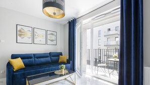 A modern living room with a blue sofa, a glass coffee table, and framed artwork on the wall. - Lumina apartment on Drewnowska (Lodz)