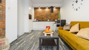 A modern living room with a yellow sofa, a coffee table with fruit, and a kitchen in the background. - Lumina apartment on Drewnowska (Lodz)