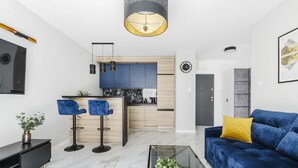 A modern living room with a blue sofa, a glass coffee table, and a kitchen in the background. - Lumina apartment on Drewnowska (Lodz)