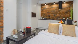 A modern hotel room with a bed, a small table with a bottle of wine, and a kitchenette in the background. - Lumina apartment on Drewnowska (Lodz)