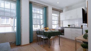 A modern kitchen with white cabinets, a dining table with chairs, and a TV mounted above the counter. - Amazing Flat in Downtown Porto by HostWise (Porto)