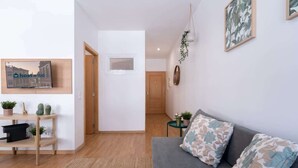 A modern living room with a grey sofa, floral cushions, a wooden coffee table, and a TV on a shelf. - Amazing Flat in Downtown Porto by HostWise (Porto)