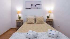 A hotel room with a bed, two bedside tables with lamps, a wall-mounted picture, and two rolled towels with a logo. - Amazing Flat in Downtown Porto by HostWise (Porto)