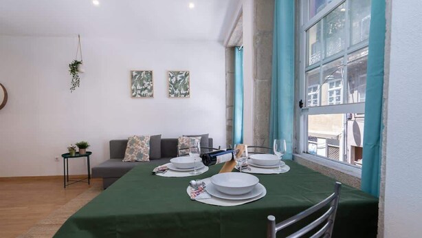 A dining area with a table set for four, a sofa, and a small side table with a plant. - Amazing Flat in Downtown Porto by HostWise (Porto)