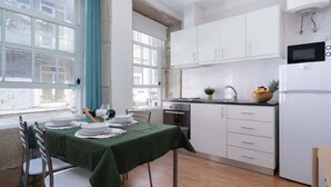 A modern kitchen with white cabinets, a microwave, and a sink. There is a dining table set with plates and a bowl of fruit. - Amazing Flat in Downtown Porto by HostWise (Porto)