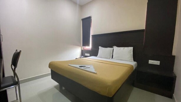 A hotel room with a bed, a chair, a bedside table, and a window with blinds. - Hotel Lebanon INN (Tirupporur)