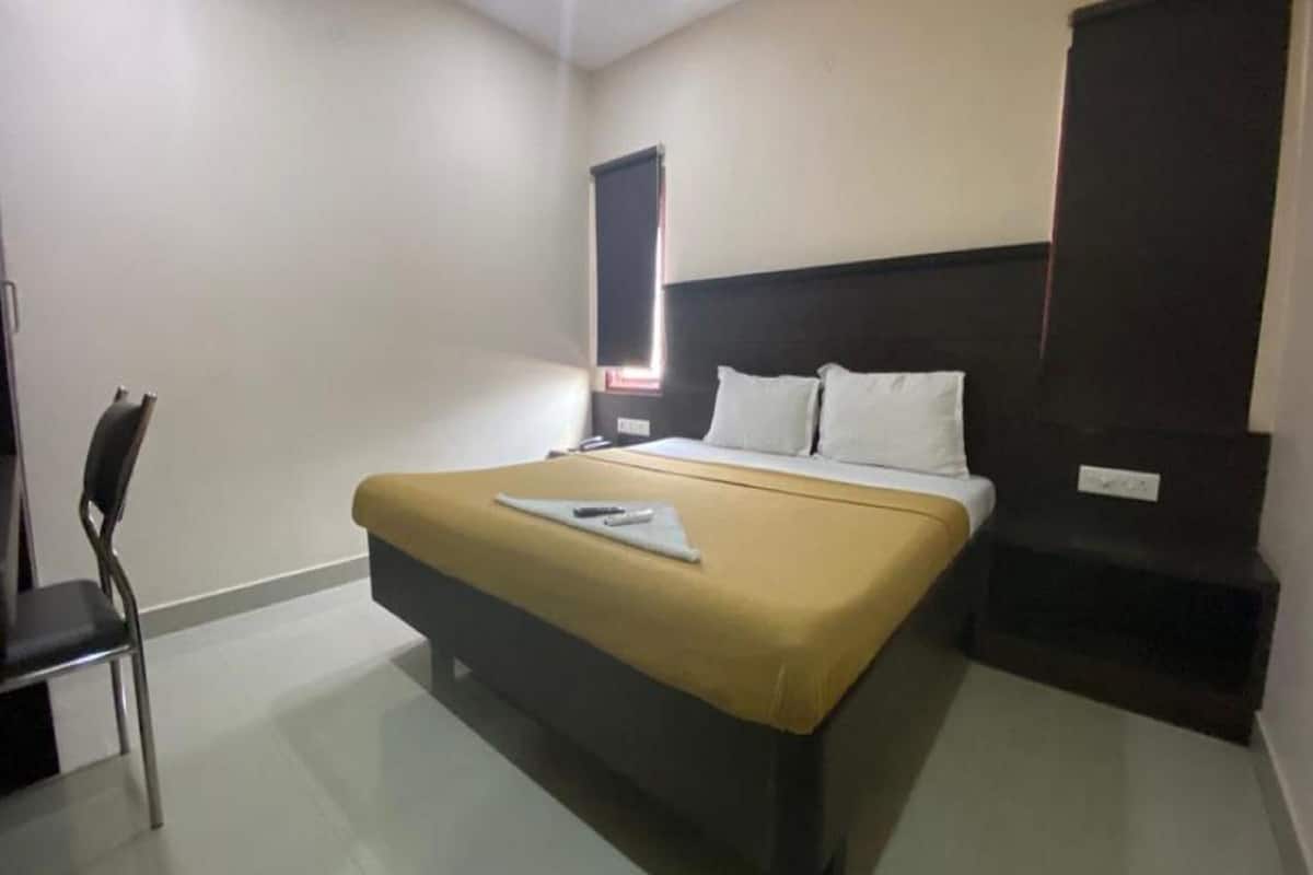 A hotel room with a bed, a chair, a bedside table, and a window with blinds.