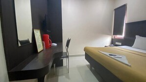 A hotel room with a bed, a desk with a chair, a red mug, and a television. - Hotel Lebanon INN (Tirupporur)