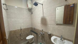 A bathroom with a toilet, bidet, sink, and a mirror. - Hotel Lebanon INN (Tirupporur)