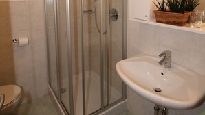 A bathroom with a glass-enclosed shower, a sink, and a mirror with lights.