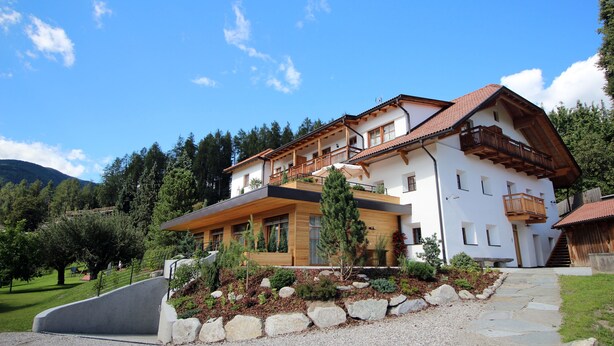 A modern two-story house with a sloped roof, wooden balconies, and a stone pathway leading to the entrance.