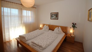 A double bed with a wooden headboard, two bedside tables with lamps, a large window with sheer curtains, and a framed picture on the wall.