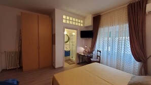 A hotel room with a bed, a desk, a chair, a TV, and a bathroom visible through an open door.