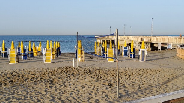 A beach with yellow and blue beach chairs and umbrellas, a wooden pier, and a concrete building with graffiti.