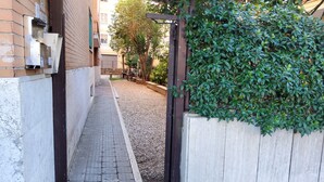 A narrow alleyway with a paved path, a wooden gate, and a hedge on one side.
