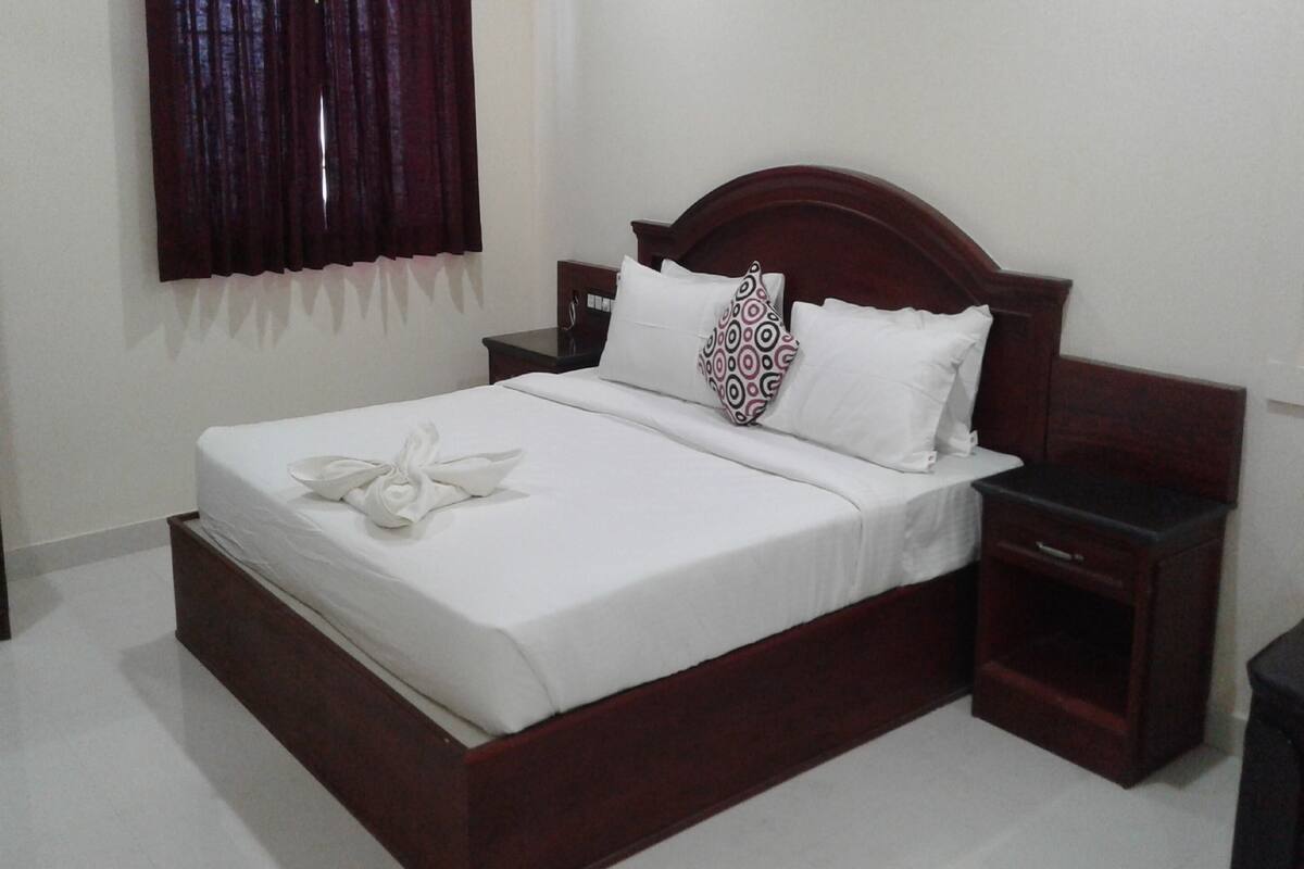 A neatly made bed with white linens and a towel, a wooden headboard, and a nightstand with a drawer.