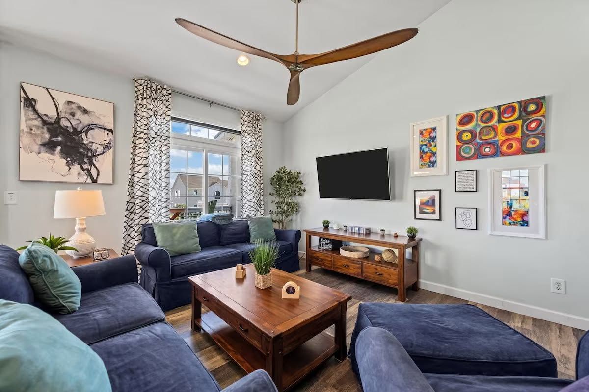 A modern living room with a ceiling fan, a flat-screen TV, and artwork on the walls.