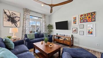 A modern living room with a ceiling fan, a flat-screen TV, and artwork on the walls.