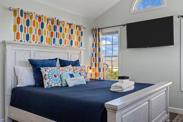 A bedroom with a bed, pillows, a TV, and a window.