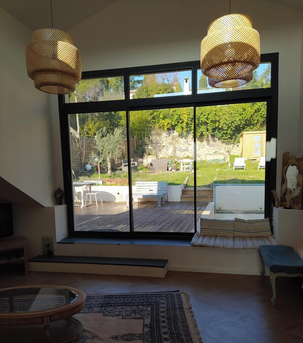 Ein Zimmer mit groĂem Fenster, Korbstuhl-Pendelleuchten, einem runden Glastisch und einem gemusterten Teppich.