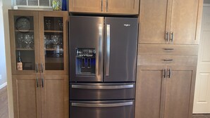 Ein Edelstahl-Kühlschrank mit integriertem Wasserspender, eine Weinflasche in einem Schrank und eine Uhr.