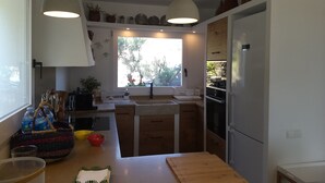 A modern kitchen with a large window, wooden cabinets, a sink, and a refrigerator. - Casa Margot 2 (Cadaqués)