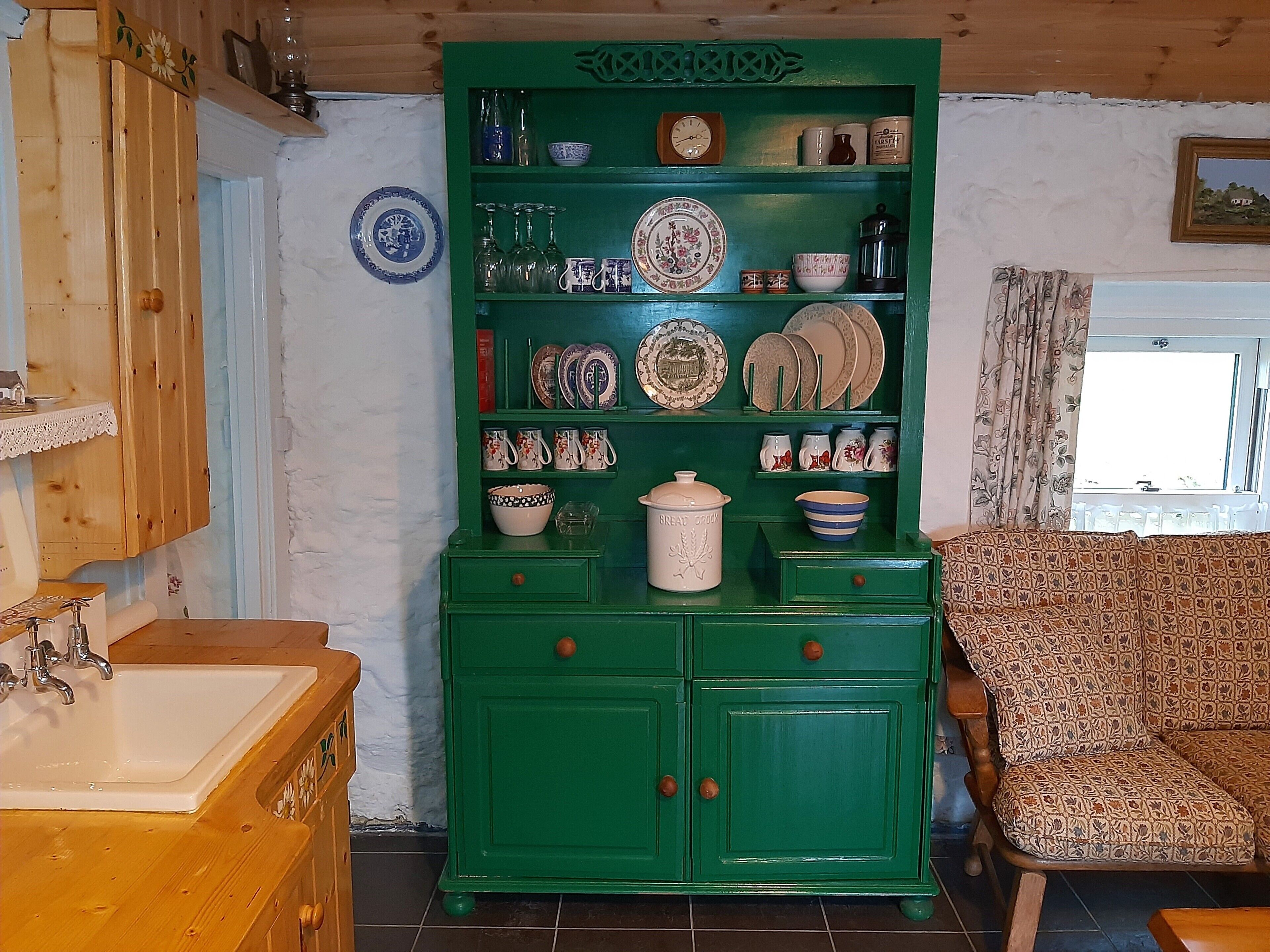 Un meuble vert contenant divers ustensiles de cuisine, un évier et un canapé à motifs.