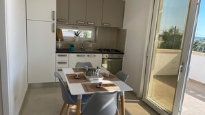 Moderni keittiö, jossa on ruokailutila. Tilaan kuuluu ruokapöytä tuoleineen, liesi ja pesuallas.