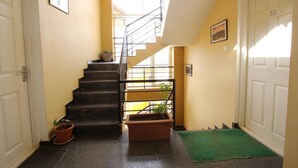 A narrow hallway with a staircase, a potted plant, and a green mat at the bottom. - The Hill Side (Ootacamund)